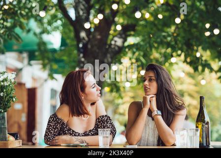 Zwei junge, schöne Freundinnen, die sich in einem Café im Freien unterhalten Stockfoto