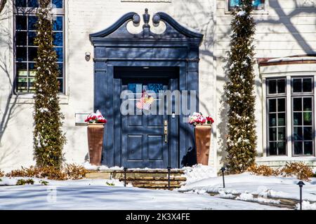 Blaue Haustür mit gebogenen und geschnitzten Rams Kopf Giebel in weißem Haus im Schnee mit Valentine Herzen Dekoration Tür.j Stockfoto