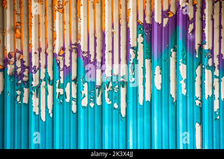 Farbenfroher Hintergrund aus türkis-violetten und orangen vertikalen Streifen - interessante abblätternde Farbe auf Wellblechwand Stockfoto