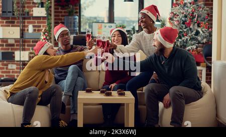 Portrait von Mitarbeitern, die während der Weihnachtsfeier im Büro Weingläser anklimmerten und auf die Feier der saisonalen Feiertage anstossen. Alkohol trinken und Jubel sagen bei Winterfestlichkeiten mit Dekor. Stockfoto