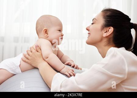 Mutter spielt mit ihrem kleinen Mädchen auf einem Fitnessball Stockfoto