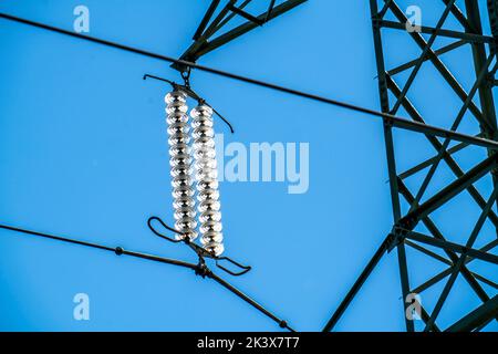 Isolatoren aus Glas an einer Hochspannungsleitung, an den Polen hängen sie als Aufhängevorrichtung zwischen dem Mast und dem stromführenden, nicht isolierten Kabel, ext Stockfoto