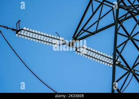 Isolatoren aus Glas an einer Hochspannungsleitung, an den Polen hängen sie als Aufhängevorrichtung zwischen dem Mast und dem stromführenden, nicht isolierten Kabel, ext Stockfoto