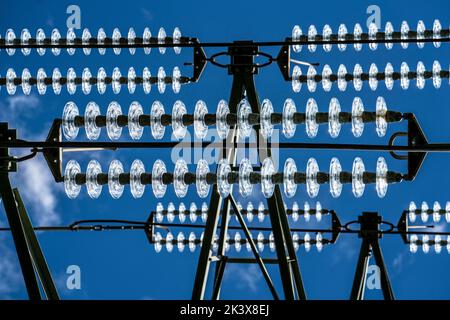 Isolatoren aus Glas an einer Hochspannungsleitung, an den Polen hängen sie als Aufhängevorrichtung zwischen dem Mast und dem stromführenden, nicht isolierten Kabel, ext Stockfoto