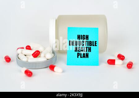 Medizinisches Konzept. Auf grauem Hintergrund ein Glas, Kapseln und ein Schild mit der Aufschrift - hoher Selbstbehalt Gesundheitsplan Stockfoto