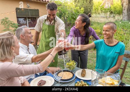 Fröhliche Familie, die mit einem wunderschönen Lächeln am Tisch im hauseigenen Patio-Diner toasting. Stockfoto