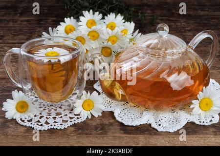 Das Konzept des medizinischen Tees. Gänseblümchen auf dem Tisch und Tee in einer Glas-Teekannen und Tasse. Stockfoto