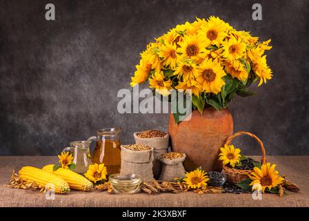 Stillleben mit Sonnenblumen und Früchten der Ernte. Dornen aus Weizen, Mais, Sonnenblumen und Maisöl. Samen in einem Korb. Stockfoto