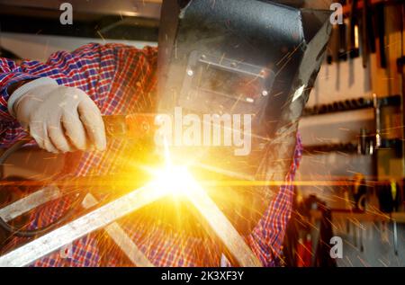 Schweißen von Metallkonstruktionen mit Blitzlicht und Funken. Schweißer bei der Arbeit. Schlosser mit einer Elektrode in der Hand. Metallverarbeitung Produktionsfabrik. Heav Stockfoto