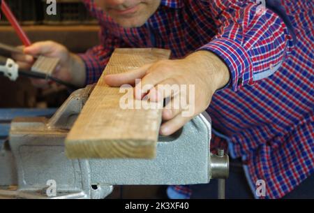 Der Zimmermann in der Werkstatt bereitet eine Schneidebrett vor. Tischlerarbeiter in der Schreinerei. Ein sorgfältiger Experte und sorgfältiger Handwerker, der sich auf die Arbeit konzentriert. Stockfoto