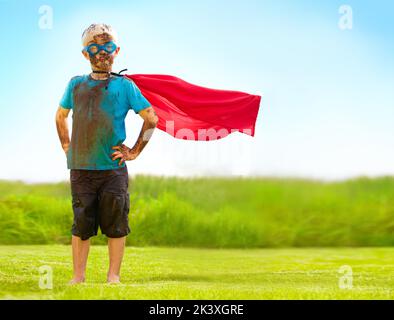 Ein schlammiger Superheld. Ein kleiner Junge, der als Superheld verkleidet und mit Schlamm bedeckt ist. Stockfoto