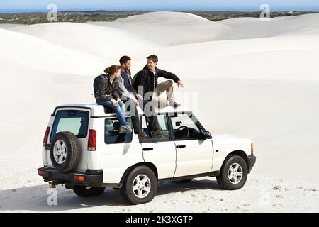 Eine Gruppe von Freunden, die auf einem Roadtrip auf ihrem Auto sitzen. Stockfoto