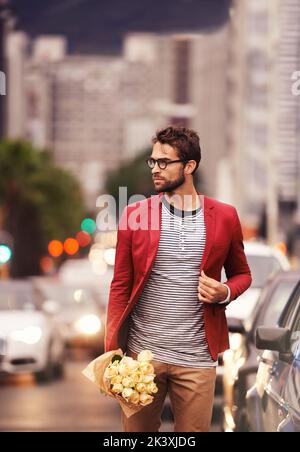 Ein hübscher junger Mann, der mit einem Blumenstrauß in der Hand durch die Stadt läuft. Stockfoto