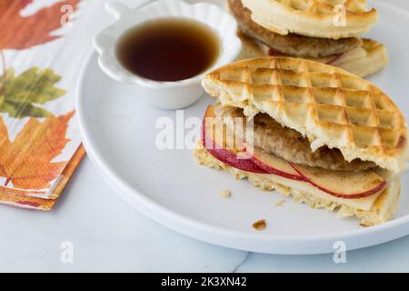 Ein Waffel- und Würstensandwich auf einem Teller serviert mit Ahornsirup zum Eintauchen. Stockfoto