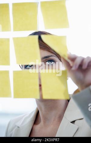 Visualisieren ihrer Gedanken. Eine Geschäftsfrau arrangiert Haftnotizen auf einem Glaswal. Stockfoto