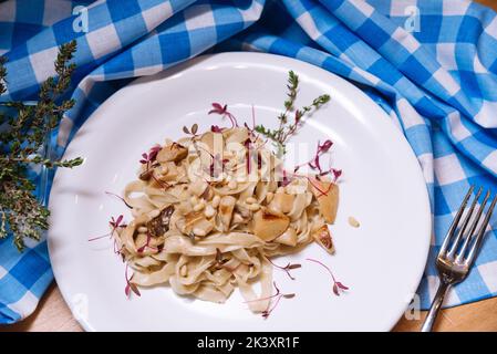 Tagliatelle Pasta in cremiger Sauce mit Steinpilzen auf einem weißen Teller und einer karierten blau-weißen Serviette Stockfoto