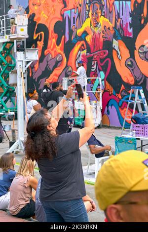 Beim RVA Street Art Festival im Kraftwerk entlang des Canal Walk von Richmond VA beobachten Besucher die Entstehung neuer Wandgemälde. Stockfoto