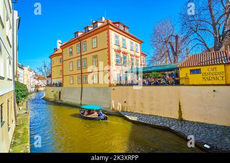 PRAG, TSCHECHISCHE REPUBLIK - 12. MÄRZ 2022: Kleines Boot fährt entlang des Certovka-Kanals zwischen mittelalterlichen Herrenhäusern und beliebten Restaurants, am 12. März in Prag, Stockfoto