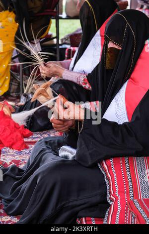 Maskierte arabische Frau aus Abu Dhabi trägt eine Abaya bei einem Folklife Festival, das traditionelle Handwerkskunst demonstriert und Wolle auf eine Spindel setzt. Stockfoto