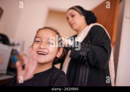 Weitergabe von Traditionen. Eine Mutter, die ihrer Tochter hilft, legt ein Kopftuch an. Stockfoto