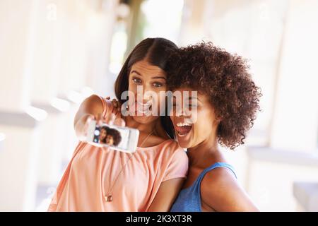 Alle lächeln, wenn Freunde abhängen. Zwei Freundinnen machen ein Selfie auf einem Handy. Stockfoto