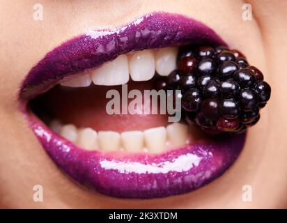 Eine Frau, die einen lila Lippenstift trägt und in eine Brombeere beißt. Stockfoto