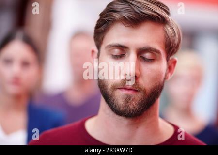 Innere kreative Vision. Ein Büroangestellter, der mit geschlossenen Augen und Kollegen im Hintergrund steht. Stockfoto