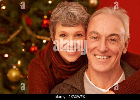 Eine Zeit, um die Angehörigen zu schätzen. Ein zugeschnittenes Porträt eines glücklichen älteren Paares vor einem Weihnachtsbaum. Stockfoto