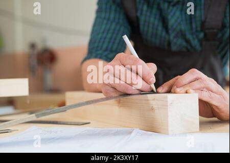 Ein Zimmermann mißt Holzbohlen und macht in einer Werkstatt mit einem Bleistift Markierungen. Stockfoto