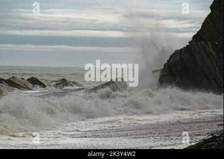 Ein steiniger Strand hat ein felsiges Ende mit Wellen, die gegen ihn krachen Stockfoto
