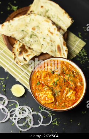 Paneer Butter Masala serviert mit Naan-Brot, Zwiebelringen und Zitrone, auf schwarzem Hintergrund mit Platz für Text, Indian Curry Stockfoto