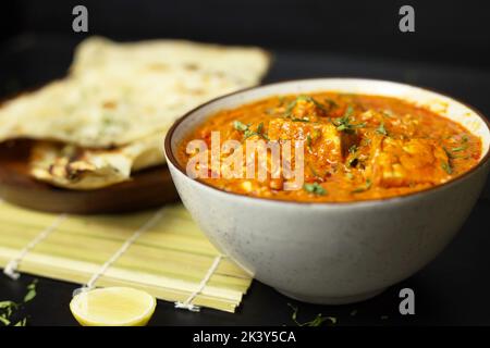 Paneer Butter Masala serviert mit Naan-Brot, Zwiebelringen und Zitrone, auf schwarzem Hintergrund mit Platz für Text, Indian Curry Stockfoto