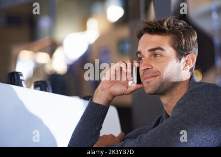 Einen Freund für Kaffee anrufen. Ein junger Mann spricht auf seinem Handy, während er in einem Café sitzt. Stockfoto