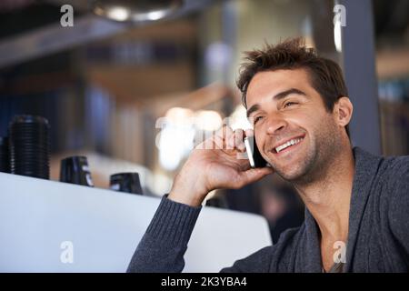 Einen Freund für Kaffee anrufen. Ein junger Mann spricht auf seinem Handy, während er in einem Café sitzt. Stockfoto