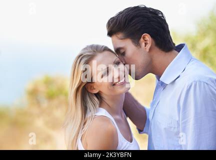 Ich kann einfach genug von Euch bekommen. Ein hübscher junger Mann, der seiner Freundin einen Kuss gibt, während sie draußen stehen. Stockfoto