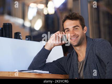 Einen Freund für Kaffee anrufen. Ein junger Mann spricht auf seinem Handy, während er in einem Café sitzt. Stockfoto