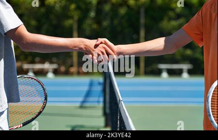 Gute Sportlichkeit. Zwei junge Tennisspieler schütteln sich die Hände über das Netz. Stockfoto