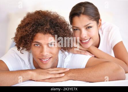 Einen entspannten Morgen teilen...Porträt eines engen jungen Paares, das im Bett liegt und die Kamera anlächelt. Stockfoto