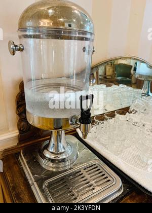 In der Hotellobby steht ein glastransparenter Tank mit einem Wasserhahn mit kaltem Trinkwasser. Nahaufnahme. Stockfoto