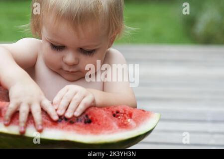 Ein Kleinkind, das seine Hände benutzt, um eine Wassermelone zu zerlegen, muss... auseinanderziehen... Stockfoto
