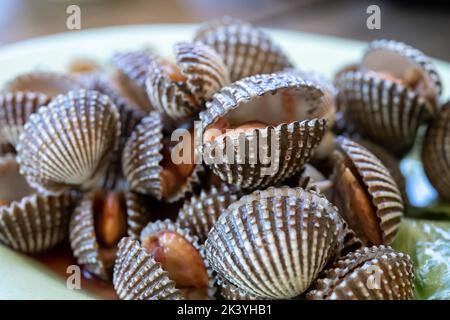 Gedünstete Herzmuscheln oder gekochte Herzmuscheln auf der Schüssel mit würzigen Meeresfrüchte-Sauce und Gemüse in Restaurante hölzernen Hintergrund Stockfoto