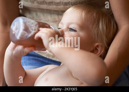 Sicher in den Armen seiner Mutter. Ein kleiner Junge trinkst aus der Flasche, während er von seiner Mutter gehalten wird. Stockfoto