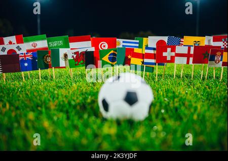 Konzeptfoto für internationales Fußballturnier. Ball auf grünem Gras und Nationalflaggen. Stadion in der Nacht. Schwarzer Hintergrund, Arbeitsbereich bearbeiten. Einschließlich Stockfoto