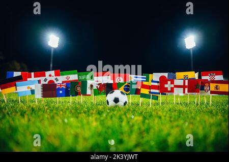 Fußball und 32 Nationalflaggen auf grünem Gras Stockfoto