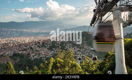 Metrocable öffentliches Nahverkehrssystem in Medellin, Kolumbien, Seilbahnen, die bei Sonnenuntergang über der Stadt fahren. Stockfoto