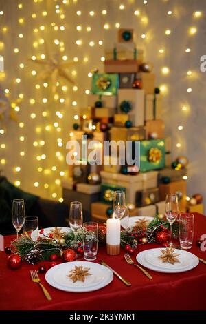 Dekorierter Tisch für Weihnachten und Neujahr mit stilvollem Tischset für vier Personen. Stapel von Geschenken im Hintergrund Stockfoto