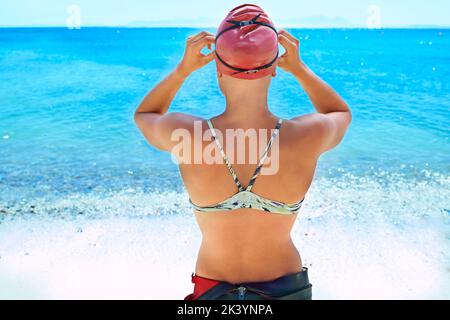 Die Arbeit an ihrem persönlichen Rekord...Rückansicht einer Schwimmerin im offenen Wasser, die sich darauf vorbereitet, in den Ozean zu gelangen. Stockfoto