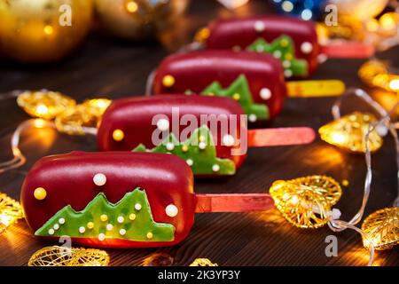 Rotes Weihnachtsdessert in Form von Mousse auf einem mit Weihnachtsbaum geschmückten Stock auf einem Hintergrund glühender Girlanden Stockfoto
