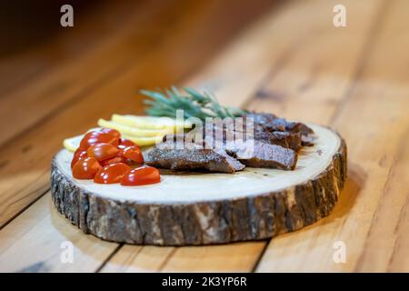 Steak Slice auf dem Holzteller, Decoration by Lemon Slice, Tomate und Rosmarin auf dem Holztisch in dezentes Licht-Ambiente. Stockfoto