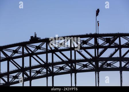 Ein Teil der Sydney Harbour Bridge, Sydney, Australien, wurde vor dem Abendhimmel geschildet. Eine Gruppe von Brückenkletterern steht an den Fahnenmasten Stockfoto